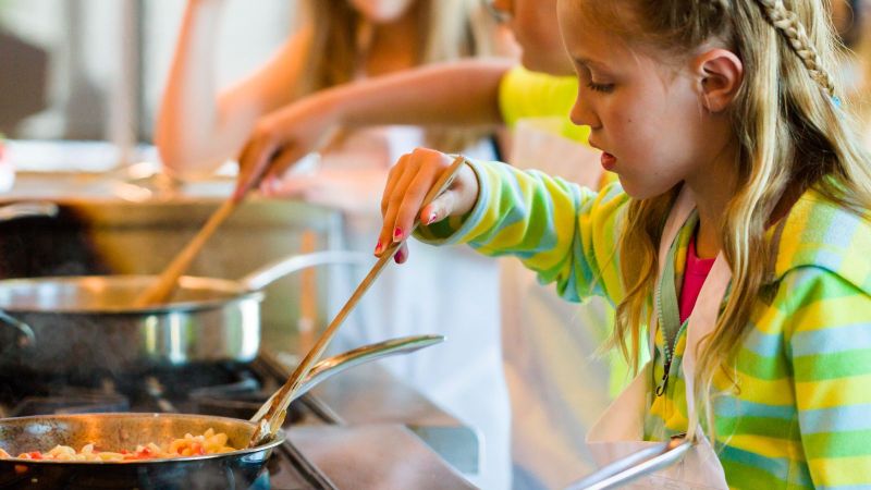 Drei Kinder rühren bei einem Kinderkochkurs in Töpfen und Pfannen.