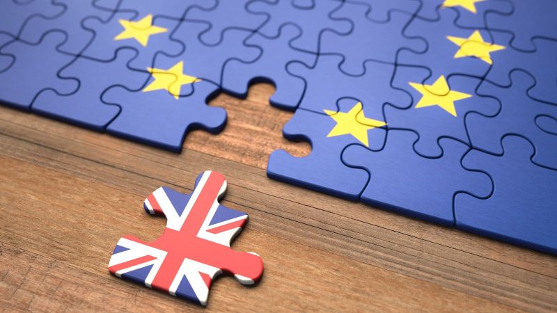 Ein Puzzle mit einer Europaflagge liegt auf einem Tisch. Ein Teil ist entfernt und zeigt die Flagge des Vereinigten Königreichs. 
