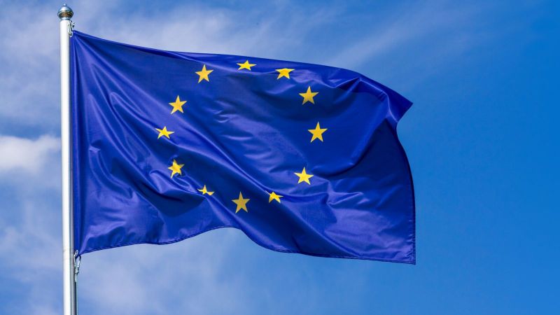 An dem Obertteil eines Fahnenmastes weht die Flagge der Europäischen Union vor blauem Himmel.