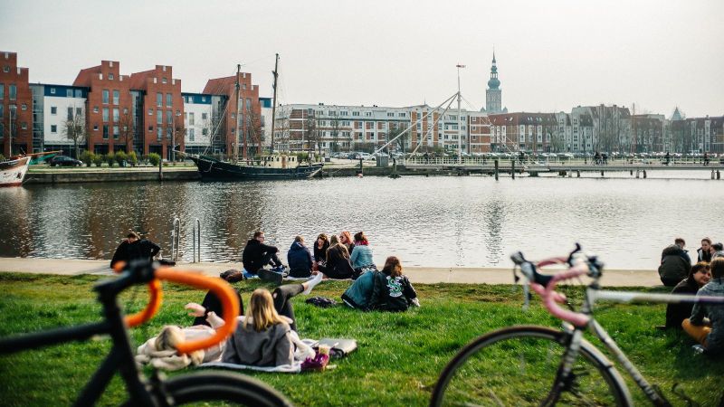 Mehrere Personengruppen sitzen auf einer Wiese am Greifswalder Hafen. Im Vordergrund stehen zwei Fahrräder.