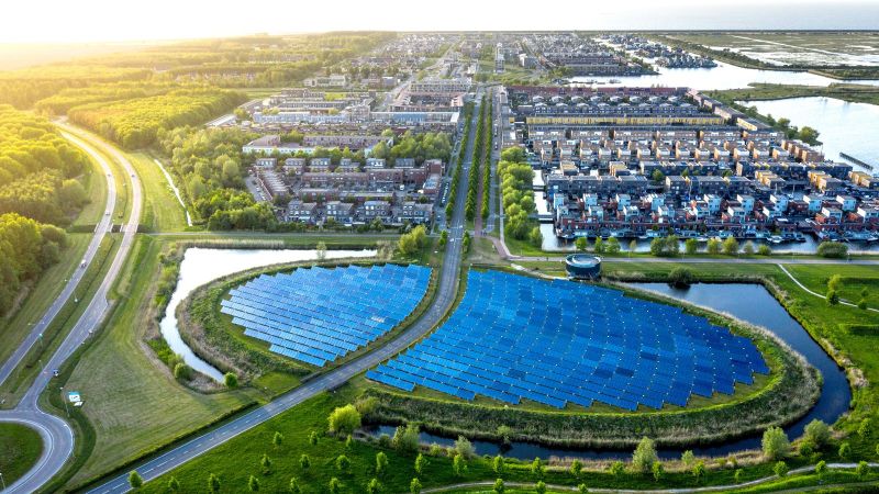 Luftaufnahme eines modernen, nachhaltigen Viertels in Almere, Niederlande. Eine große , runde Ansammlung von Solaranlagen ist im Zentrum zu sehen.