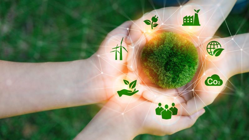 Zwei paar Hände liegen aufeinander. Darüber abstrakt ein aus Moos bestehender Kreis um den Symbole wie Windräder und CO2 angeordnet sind.
