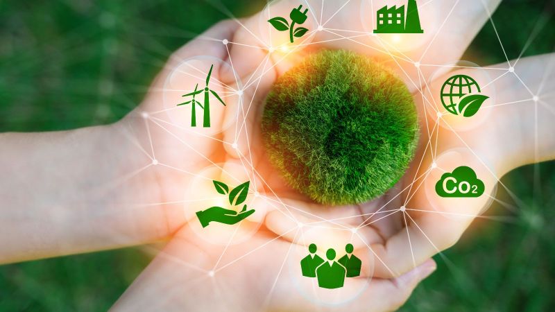 Zwei paar Hände liegen aufeinander. Darüber abstrakt ein aus Moos bestehender Kreis um den Symbole wie Windräder und CO2 angeordnet sind.