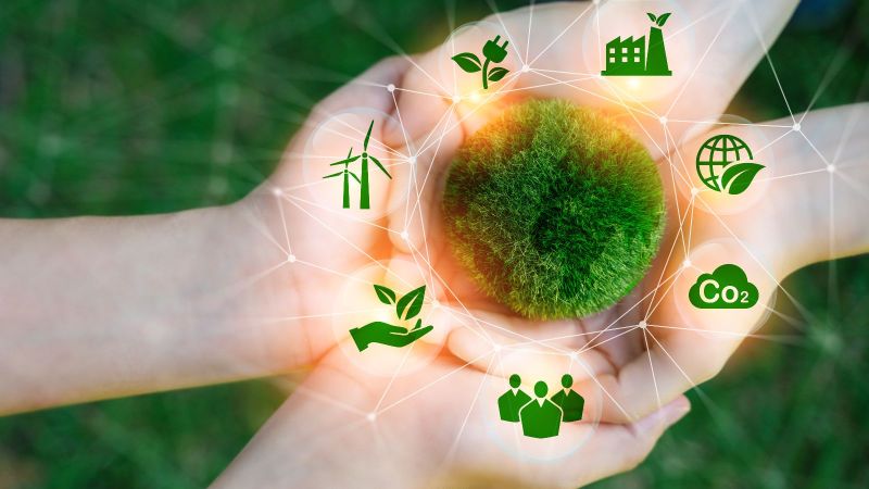 Zwei paar Hände liegen aufeinander. Darüber abstrakt ein aus Moos bestehender Kreis um den Symbole wie Windräder und CO2 angeordnet sind.