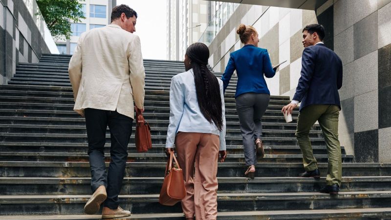 Vier Personen gehen eine Treppe hoch. Sie tragen Businesskleidung.