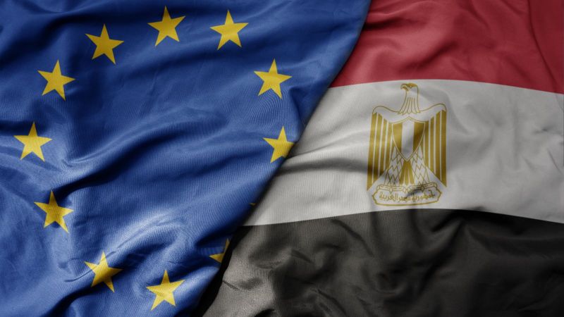 Nahaufnahme liegender, sich überlappender Flaggen. EU-Flagge links, ägyptische Flagge rechts.