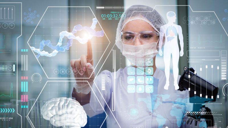 Person in medizinischer Schutzkleidung steht vor einer Hologrammgrafik mit medizinischen Daten und drückt mit ihrem FInger auf eine der Grafiken.