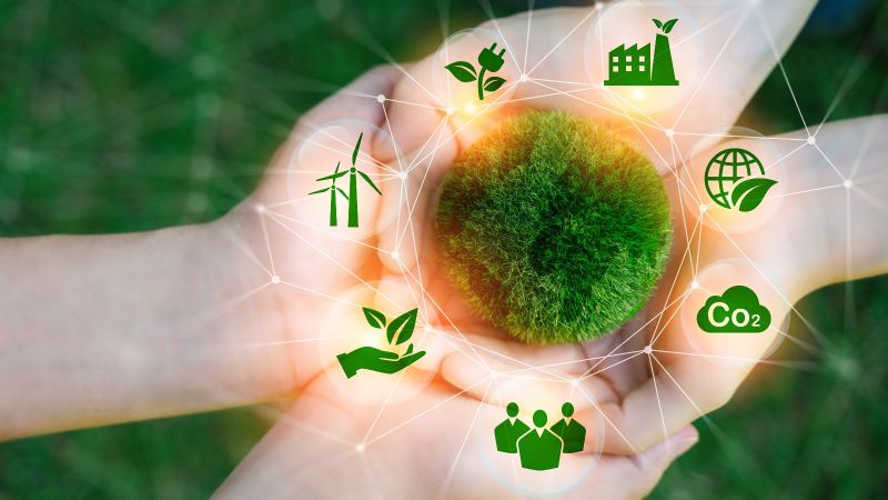 Zwei paar Hände liegen aufeinander. Darüber abstrakt ein aus Moos bestehender Kreis um den Symbole wie Windräder und CO2 angeordnet sind.