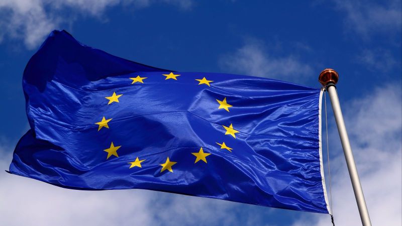 Eine Flagge der EU weht am Fahnenmast vor blauem Himmel mit weißen Wolken.