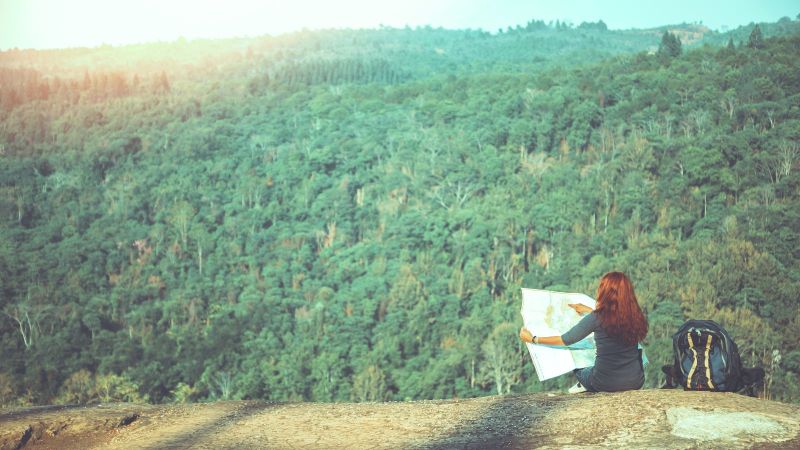 Frau sitzt vor einem Wald mit einer Karte in der Hand.