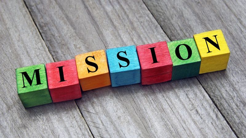 Spielklötze die auf grauem Parkett ligen und das Wort Mission bilden.