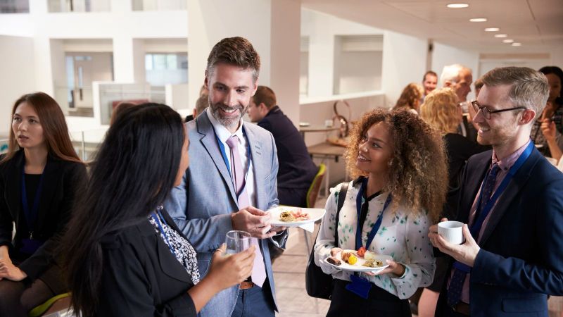 Zwei Frauen und zwei Männer sprechen miteinander und haben dabei Essen und Getränke in der Hand.