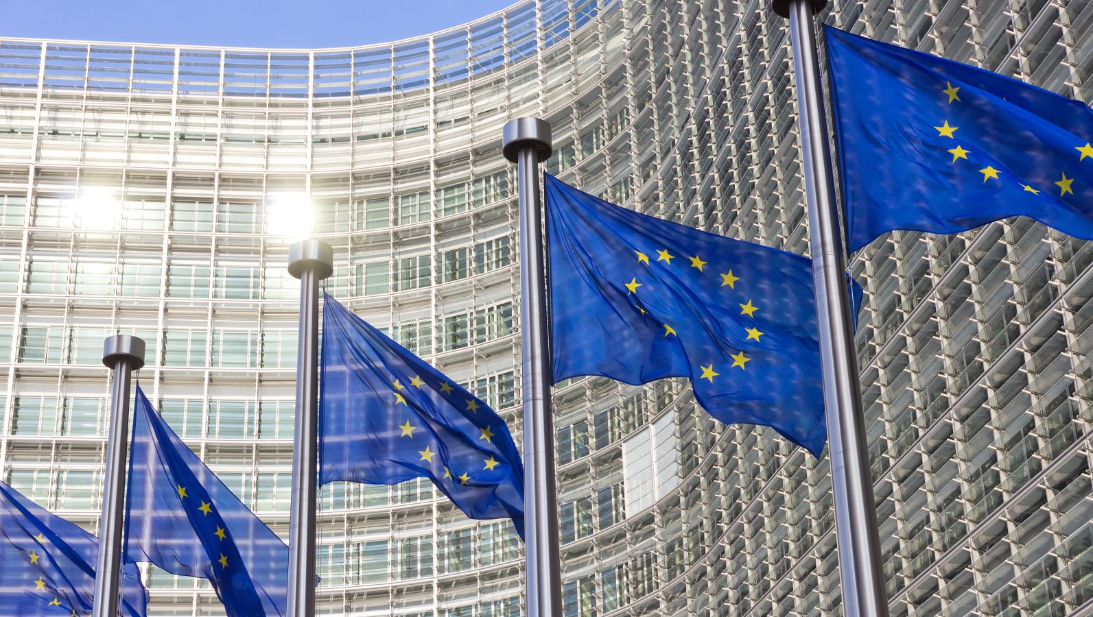 Bild des EU Kommissions Gebäude in  Brüssel mit Europa Fahnen im Vordergrund.