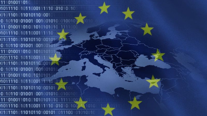 Durch eine transparente Fahne der Europäischen Union fällt der Blick auf binäre Zahlenreihen, welche sich horizontal bis in eine Karte der europäischen Mitgliedsstaaten erstrecken.