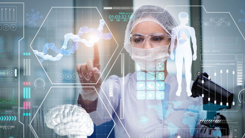 Person in medizinischer Schutzkleidung steht vor einer Hologrammgrafik mit medizinischen Daten und drückt mit ihrem FInger auf eine der Grafiken.