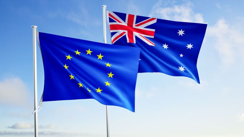 Die europäische und australische Flagge wehen nebeneinander vor sonnigem, leicht bewölktem Himmel.