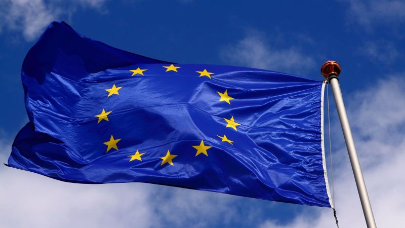 Eine Flagge der EU weht am Fahnenmast vor blauem Himmel mit weißen Wolken.