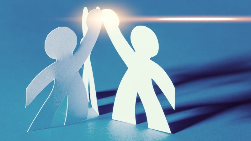 Zwei aus Papier geschnittenen Figuren klatschen über ihren Köpfen High Five ein.