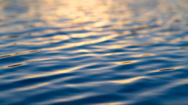 Wasseroberfläche mit sich spiegelndem Licht auf leichten Wellen.