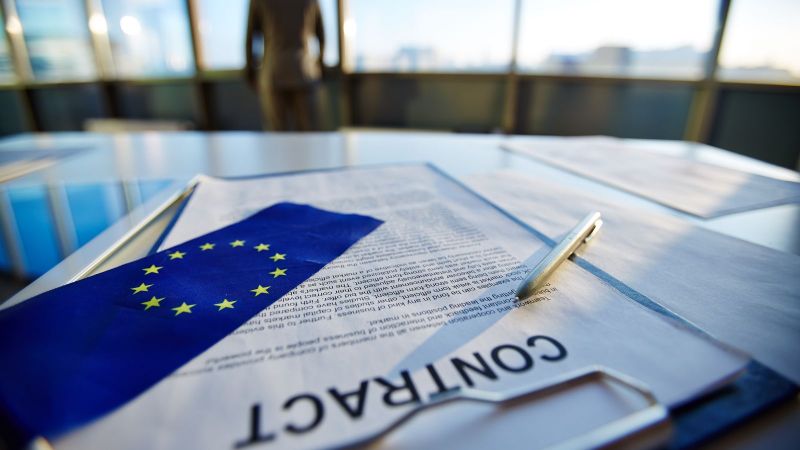 Ein Vertrag liegt auf einem Tisch. Auf dem Vertrag liegen ein Stift und eine EU-Flagge.