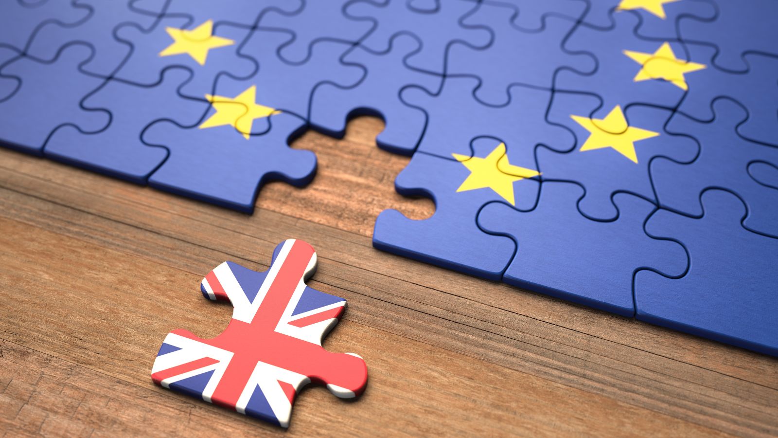 Ein Puzzle mit einer Europaflagge liegt auf einem Tisch. Ein Teil ist entfernt und zeigt die Flagge des Vereinigten Königreichs. 