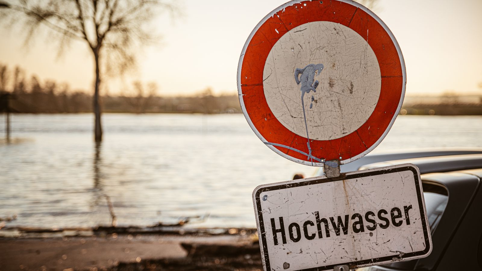 Ein Hochwasserschild blockiert den Weg zu einer überfluteten Fläche.