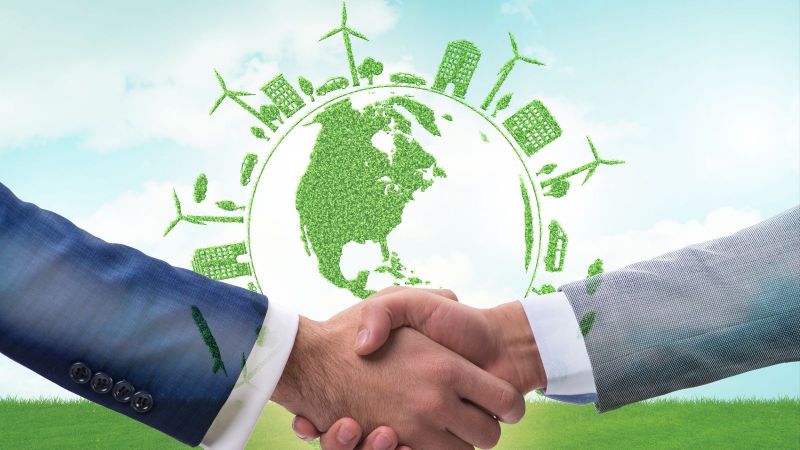 Zwei Personen in Anzügen schütteln sich die Hände. Im Hintergrund schwebt der Umriss des Globus umgeben von grünen Windkraftanlagen, Autos, Häusern und Bäumen.