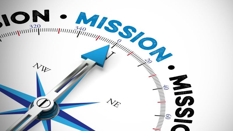 Eine blau-schwarze Kompassnadel auf weißem Untergrund zeigt auf das blaugeschriebene Wort Mission.