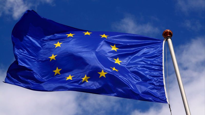 Eine Flagge der EU weht am Fahnenmast vor blauem Himmel mit weißen Wolken.