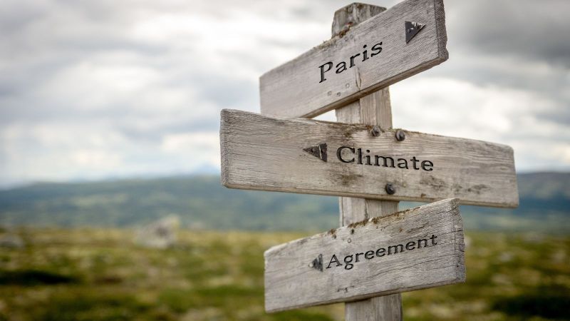Wegweiser mit den drei Schildern Paris, Climate und Agreement in hügeliger Landschaft