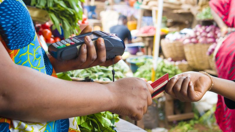 Frau mit Kartenzahlgerät an Gemüsemarktstand