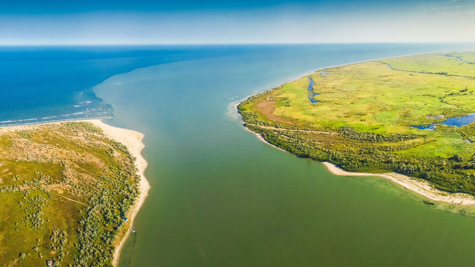 Blick aus der Vogelperspektive auf eine flache Küstenlandschaft mit grünen Wiesen und Sandstränden