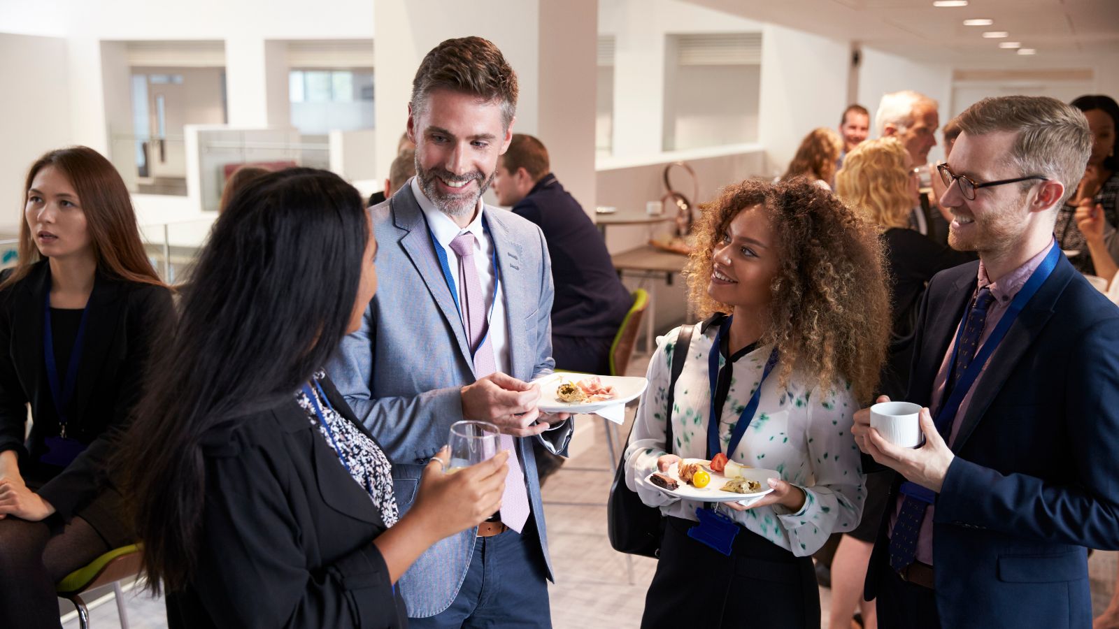Eine kleine Gruppe von Personen steht auf einem Event, gut gekleidet und mit Essen in der Hand, beieinander und unterhält sich.
