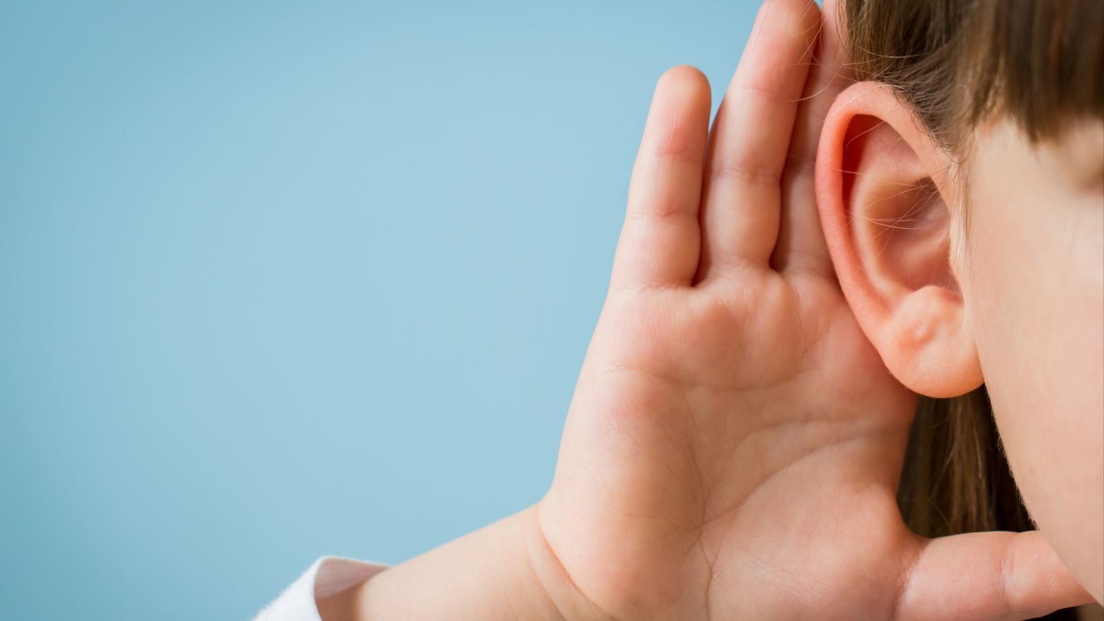 Vor blauem Hintergrund ist am rechten Bildrand in Nahaufnahme ein drittel des Gesichts eines Kindes zu sehen. Es hält sich eine Hand zum Lauschen hinter das Ohr.