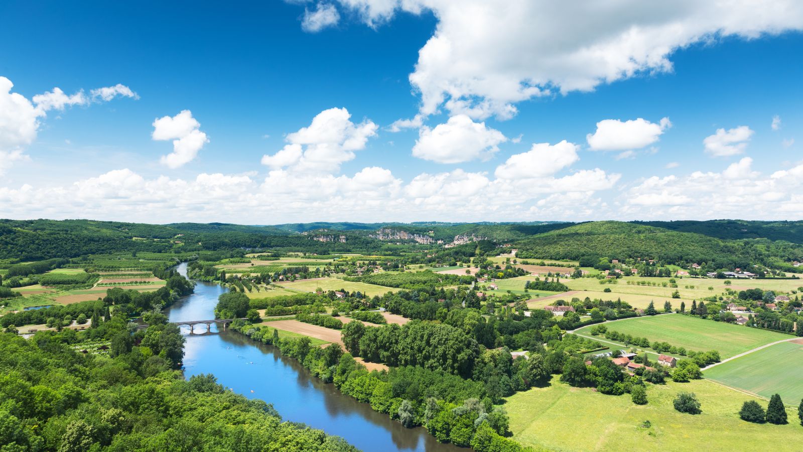 Panoramablick auf das Tal der Dordogne in Frankreich. Ein Fluss fließt durch eine Landschaft mit Feldern, Wäldern und kleineren Dörfern.