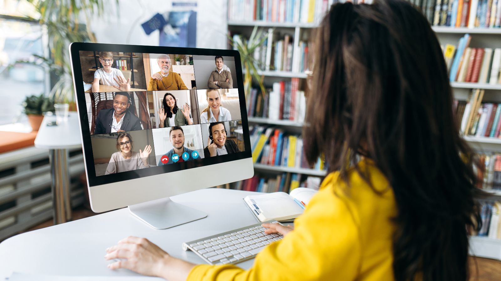 Eine Zuhörerin sitzt vor einem Bildschirm, auf dem mehrere Teilnehmer/innen einer Online-Konferenz zu sehen sind.