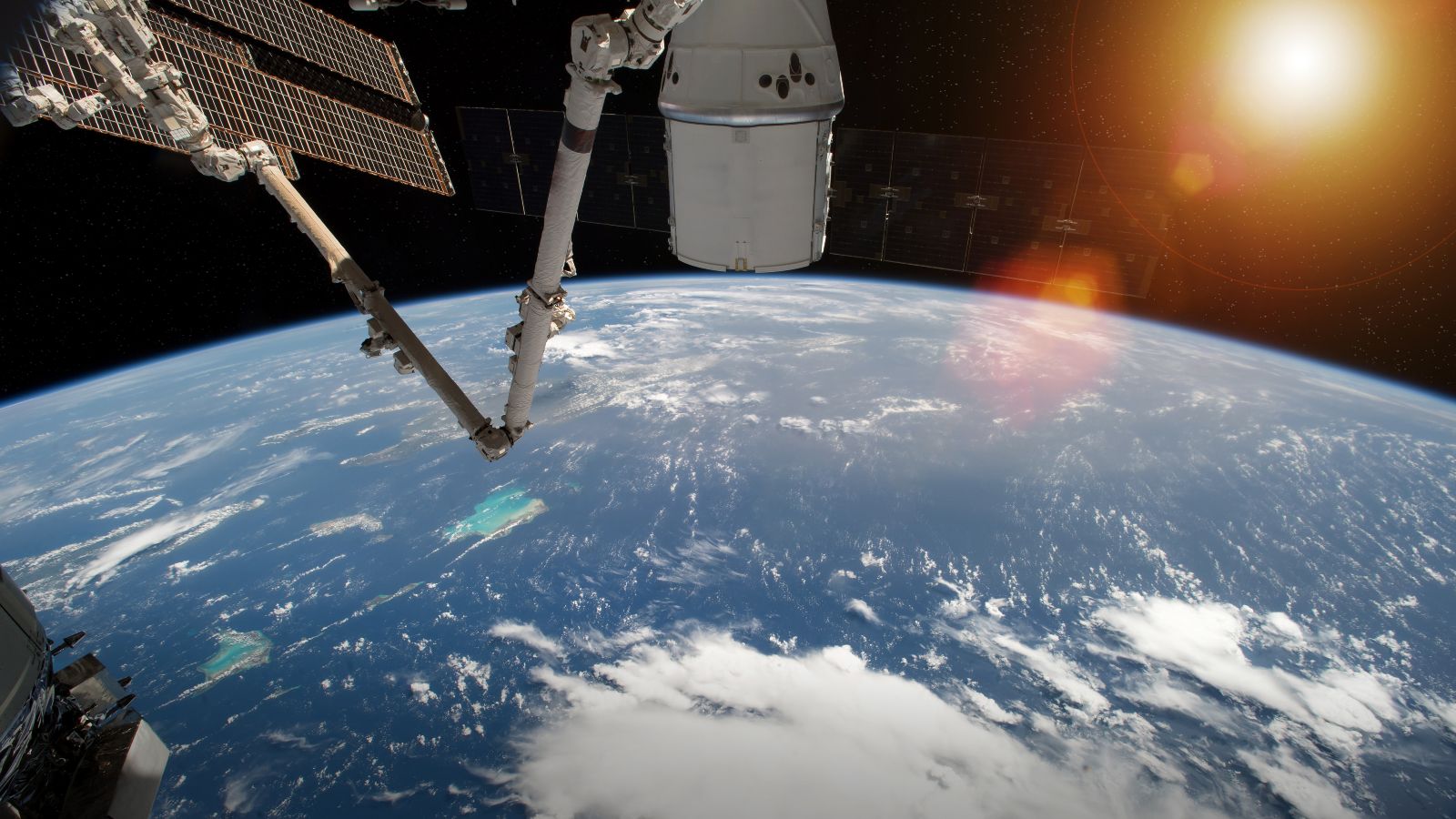 Blick auf die Erdkugel aus dem Weltall. Am Rand des Bildes sind Teile einer Raumstation und die Sonne über der Erde zu sehen.