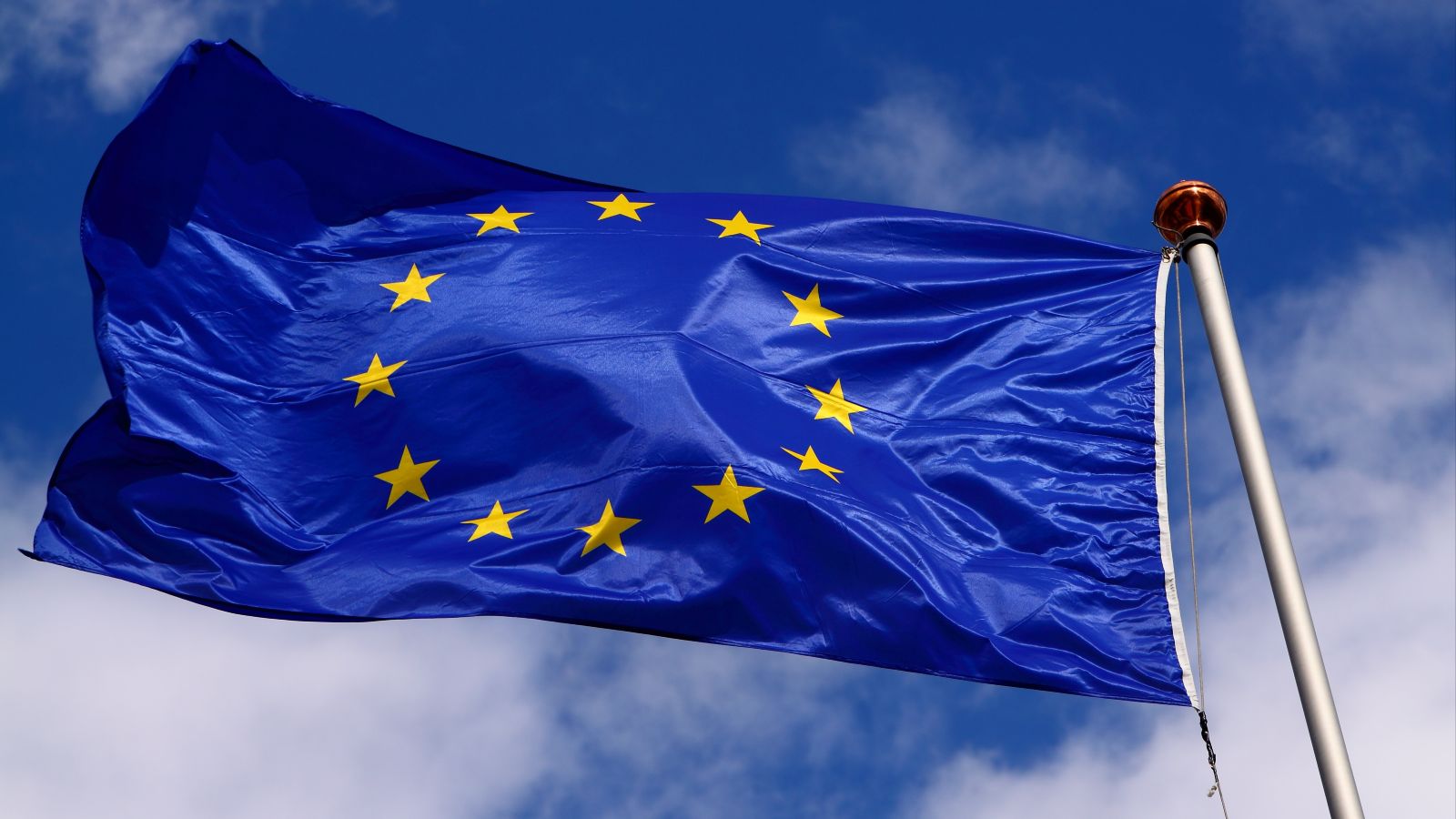 Eine Flagge der EU weht am Fahnenmast vor blauem Himmel mit weißen Wolken.