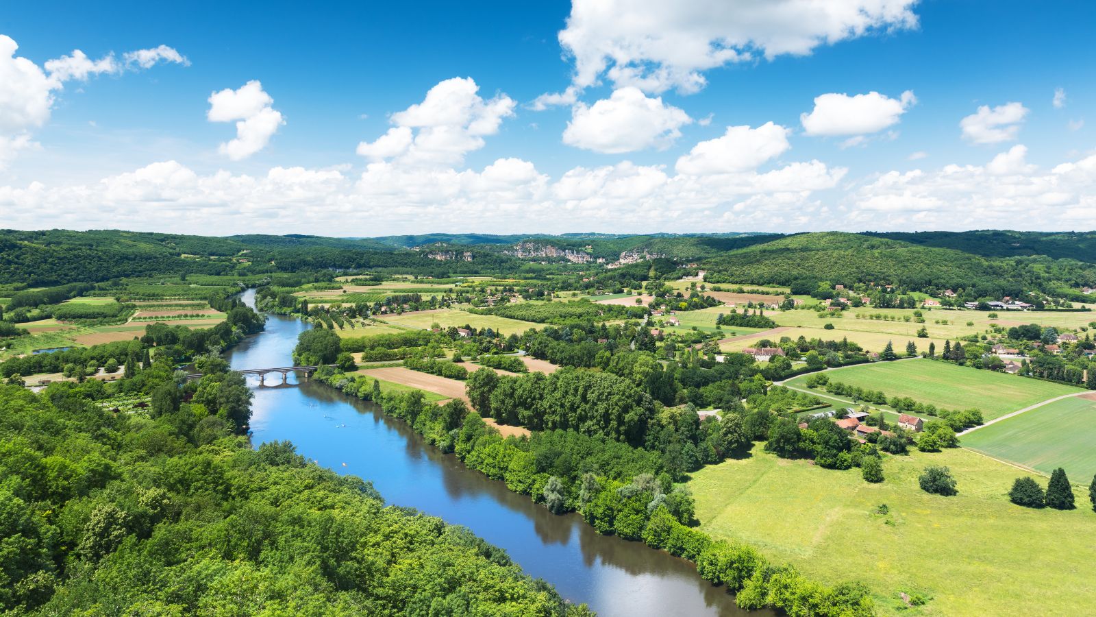 Panoramablick auf das Tal der Dordogne in Frankreich. Ein Fluss fließt durch eine Landschaft mit Feldern, Wäldern und kleineren Dörfern.