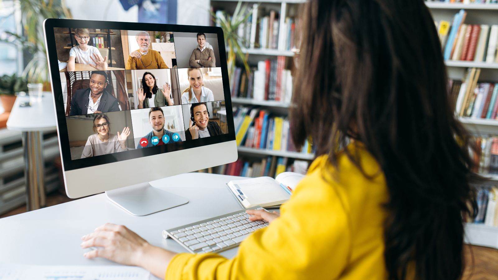 Eine Zuhörerin sitzt vor einem Bildschirm, auf dem mehrere Teilnehmende einer Online-Konferenz zu sehen sind. 