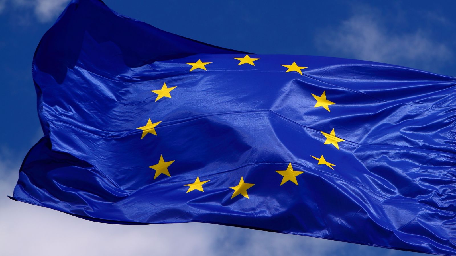 Eine Flagge der EU weht am Fahnenmast vor blauem Himmel mit weißen Wolken.