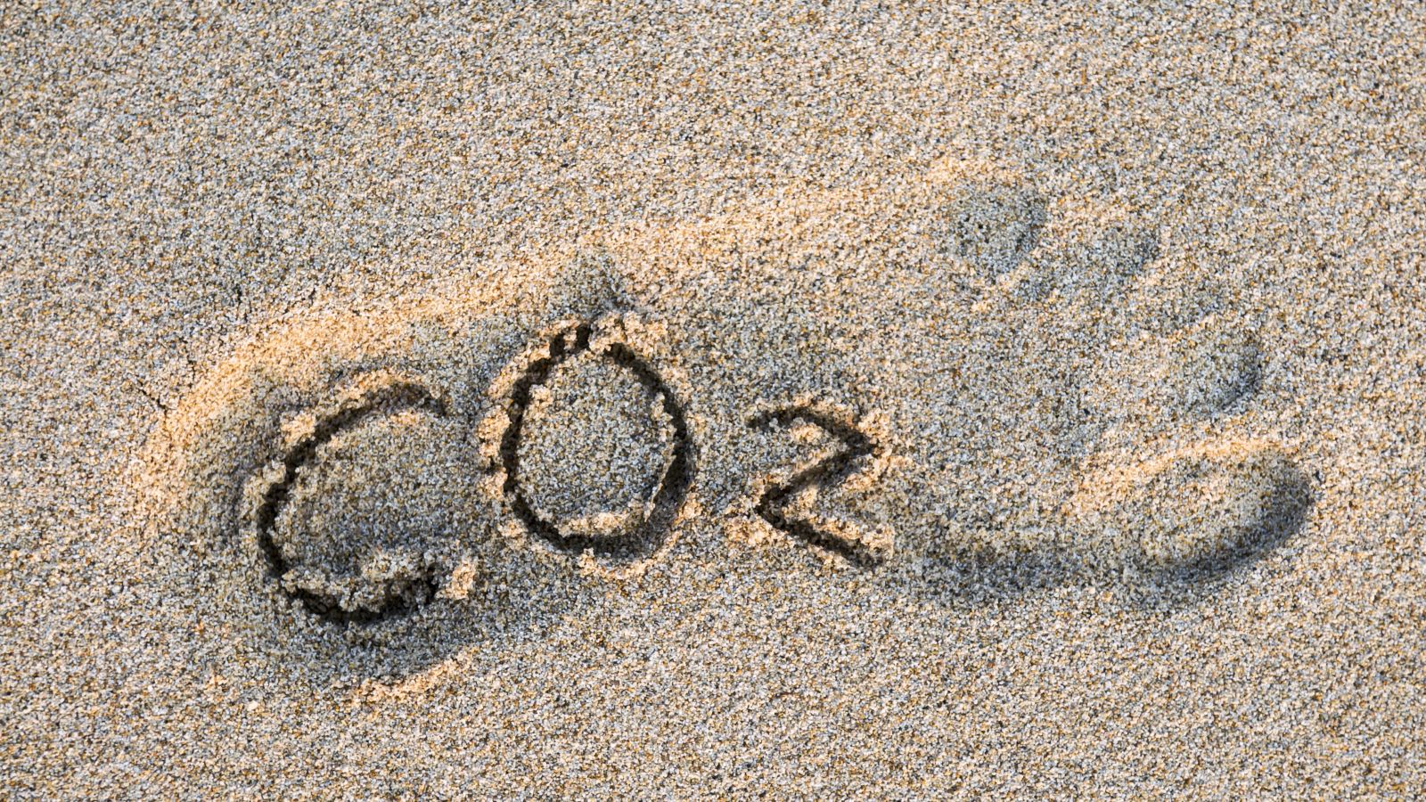 CO2-Text im Umriss eines Fußes in goldenem Sand.