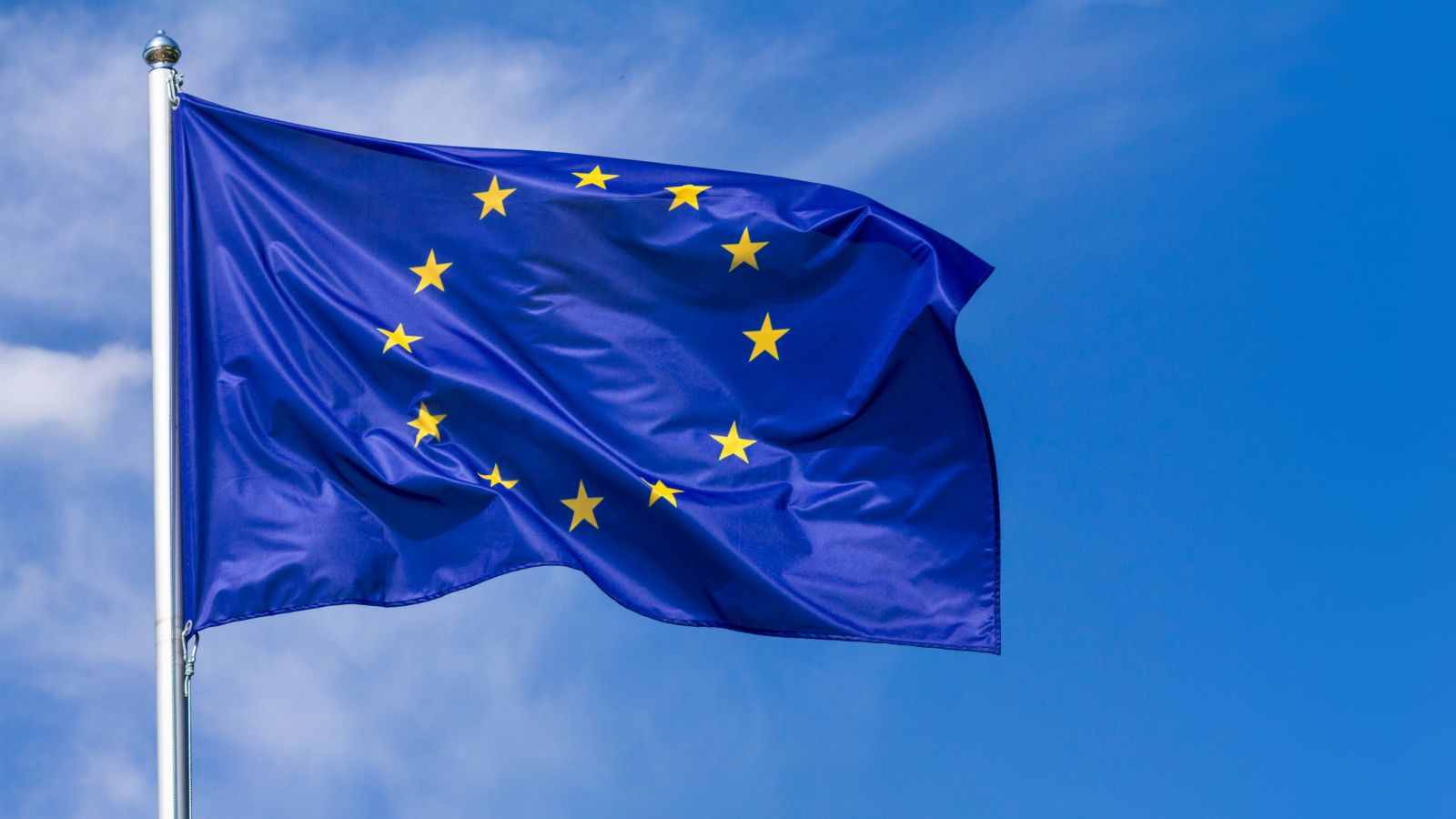 An dem Obertteil eines Fahnenmastes weht die Flagge der Europäischen Union vor blauem Himmel.