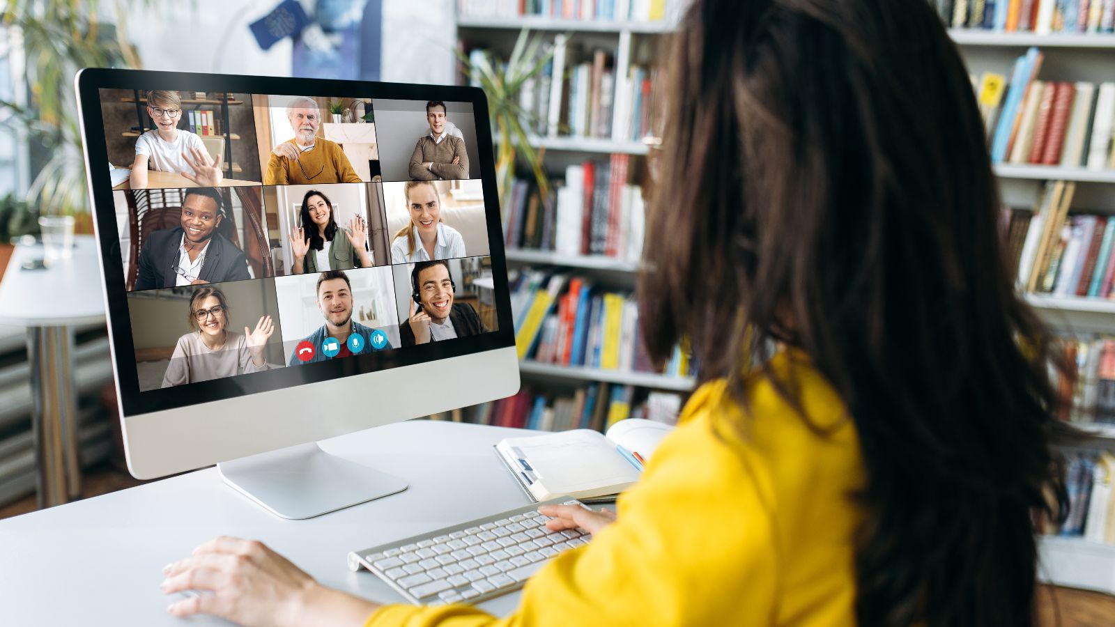 Eine Zuhörerin sitzt vor einem Bildschirm, auf dem mehrere Teilnehmende einer Online-Konferenz zu sehen sind.