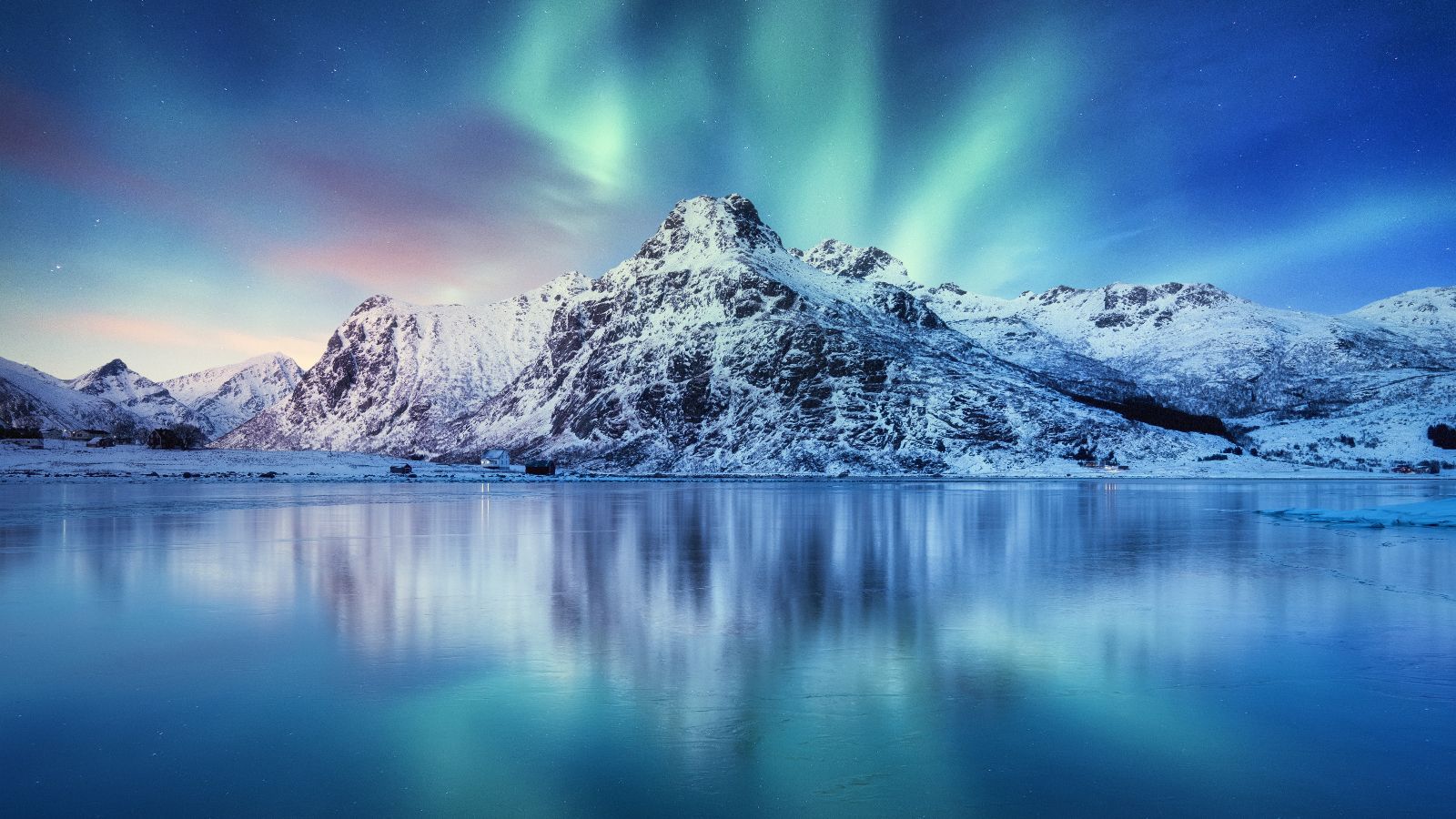 Vor einem stillen Wasser steht ein schneebedeckter Berg. Dahinter sind Nordlichter zu sehen.