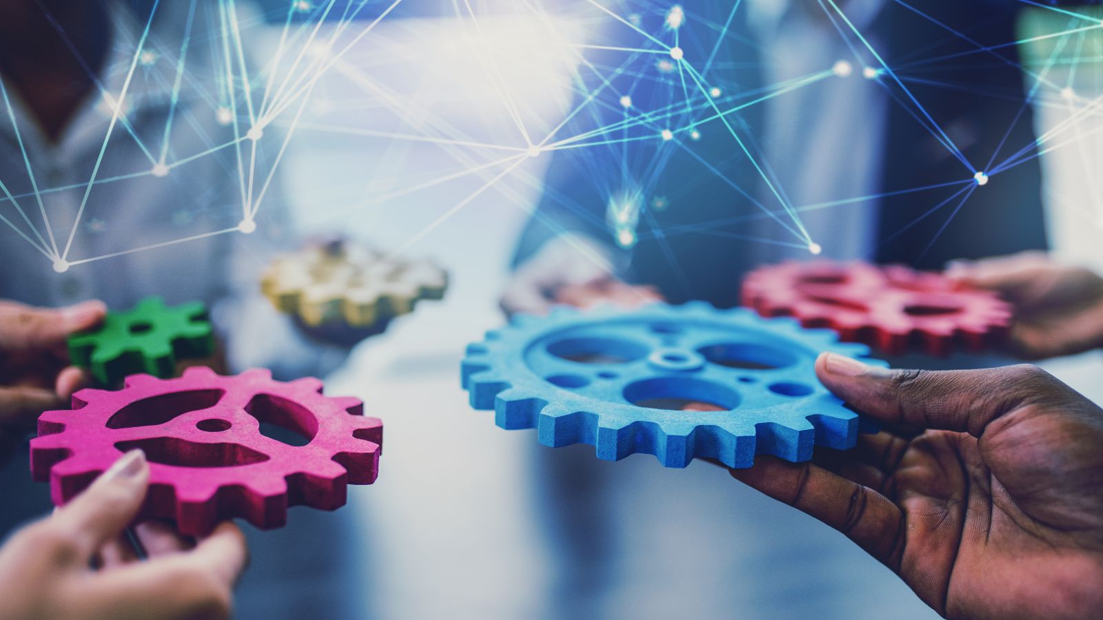 Hände unterschiedlicher Hautfarbe halten verschieden farbige Zahnräder in die Mitte. Darüber befinden sich zu einem Netz verbundene helle Punkte.