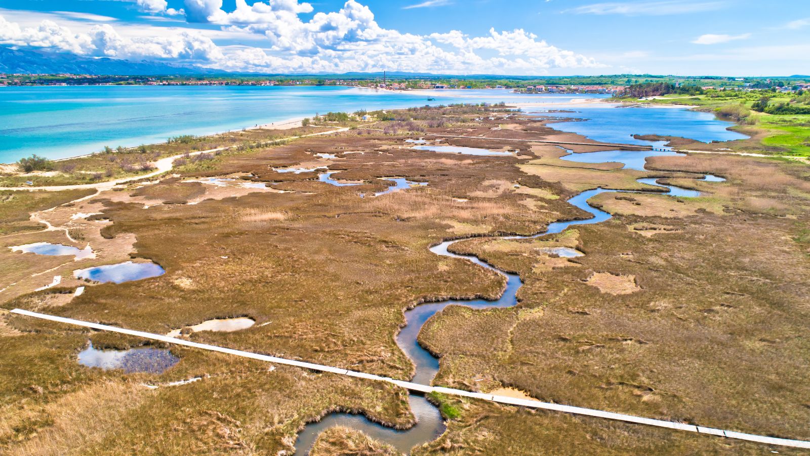 Ein Fluss schlängelt sich durch Marschland auf das Meer zu. Im Delta liegt eine Gemeinde.