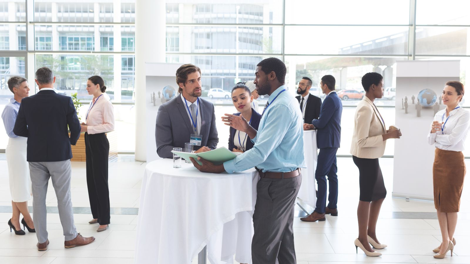 Gruppen von zwei oder drei Personen stehen in einem verglasten Raum und unterhalten sich.