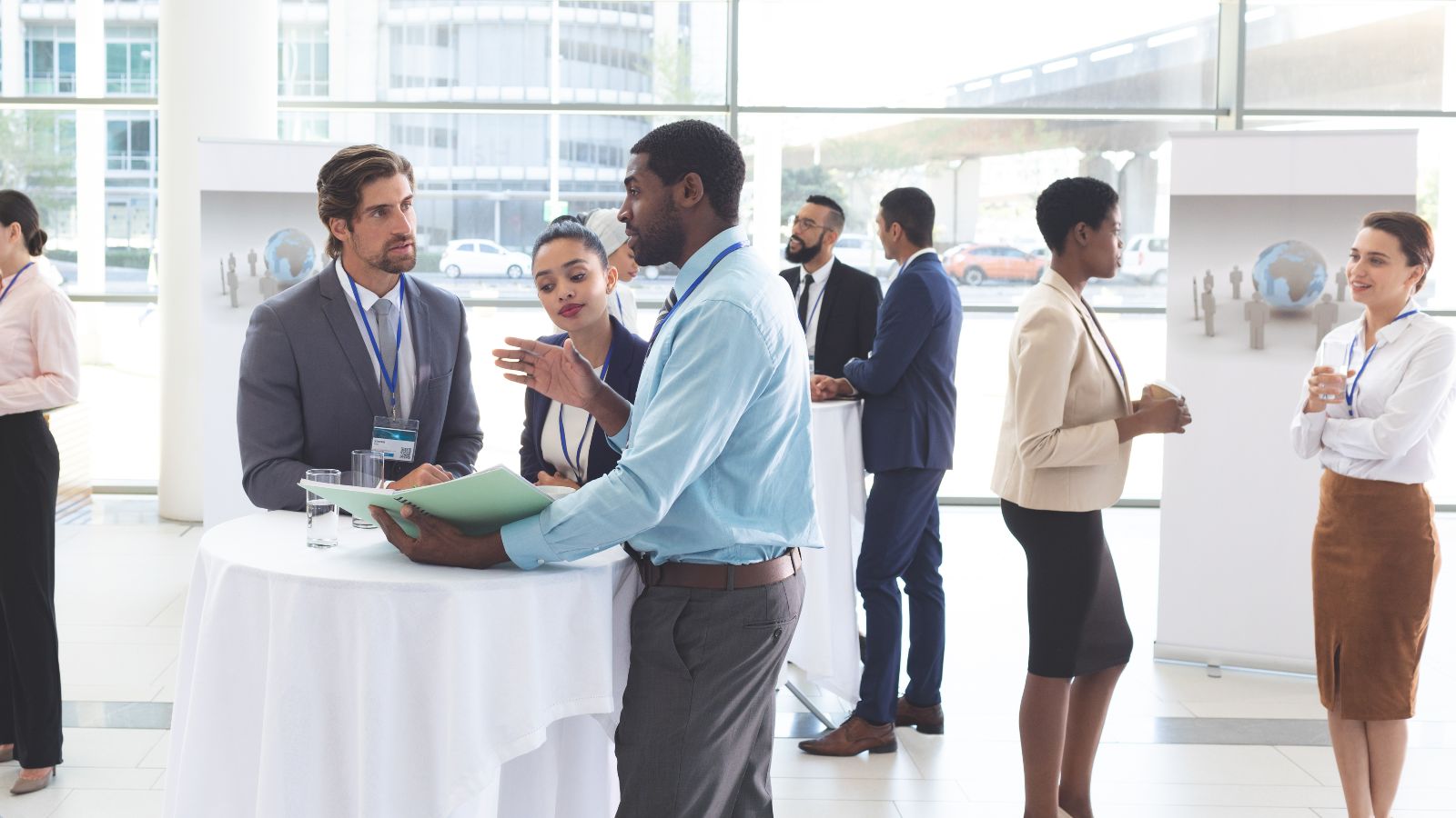 Gruppen von zwei oder drei Personen stehen in einem verglasten Raum und unterhalten sich.