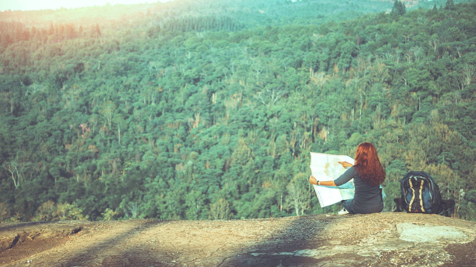 Frau sitzt vor einem Wald mit einer Karte in der Hand.